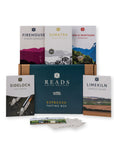 A coffee tasting box set from Reads Coffee Artifacts, featuring a dark teal box in the center surrounded by five single-variant coffee bag packages (Firehouse, Sumatra, Casa di Montagna, SideLock, and Limekiln) and a small card deck in front, all arranged on a white background.
