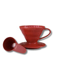A red Hario V60 pour-over coffee dripper with its matching saucer and small measuring scoop, shown on a clean white background.