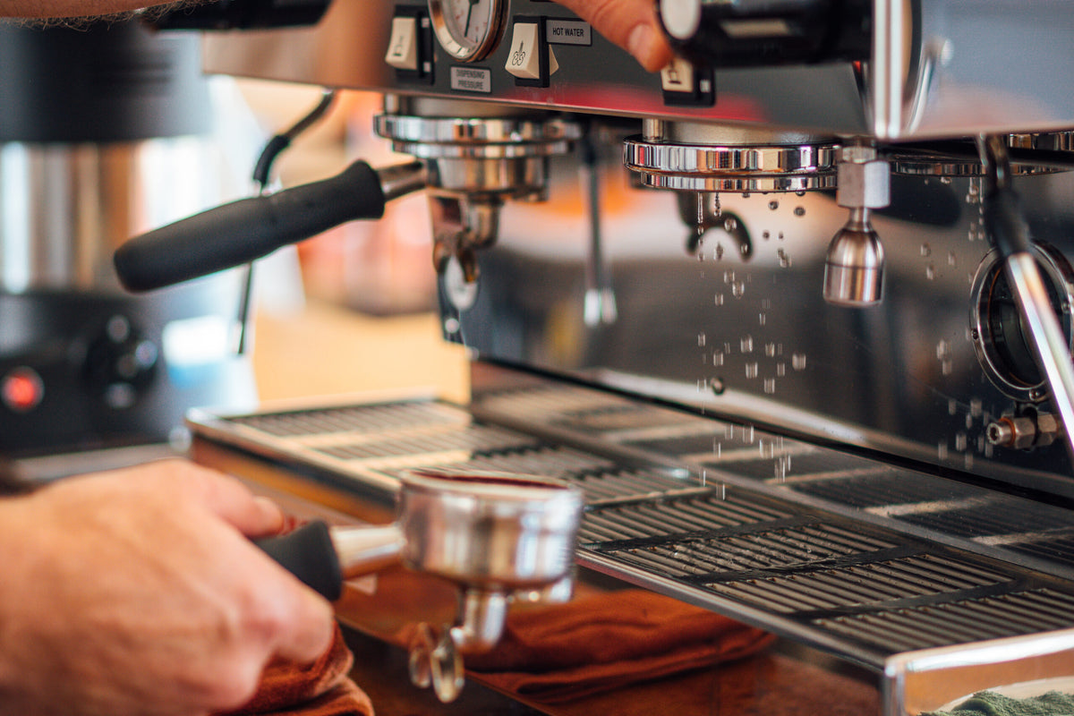 Espresso machine with a hand holding a portafilter, preparing coffee.