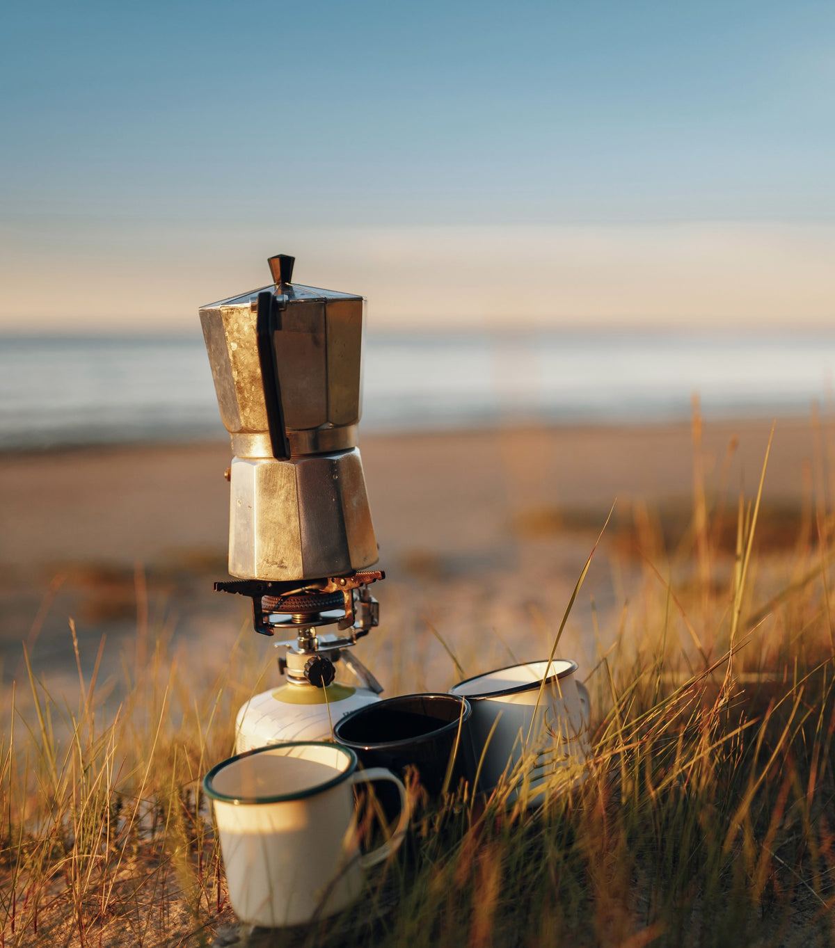 Coffee maker with cups on a beach at sunset