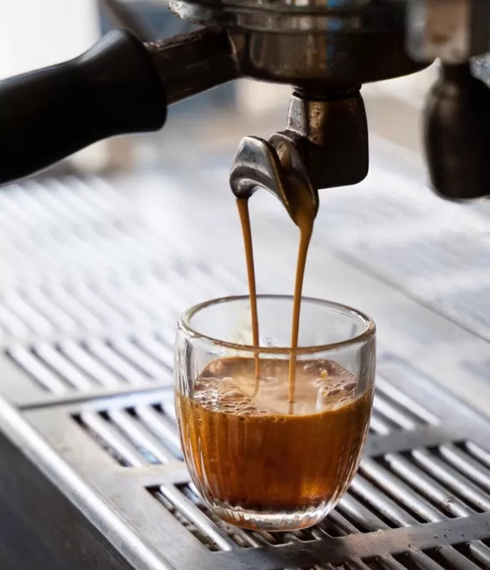 Espresso being poured from a machine into a glass cup.