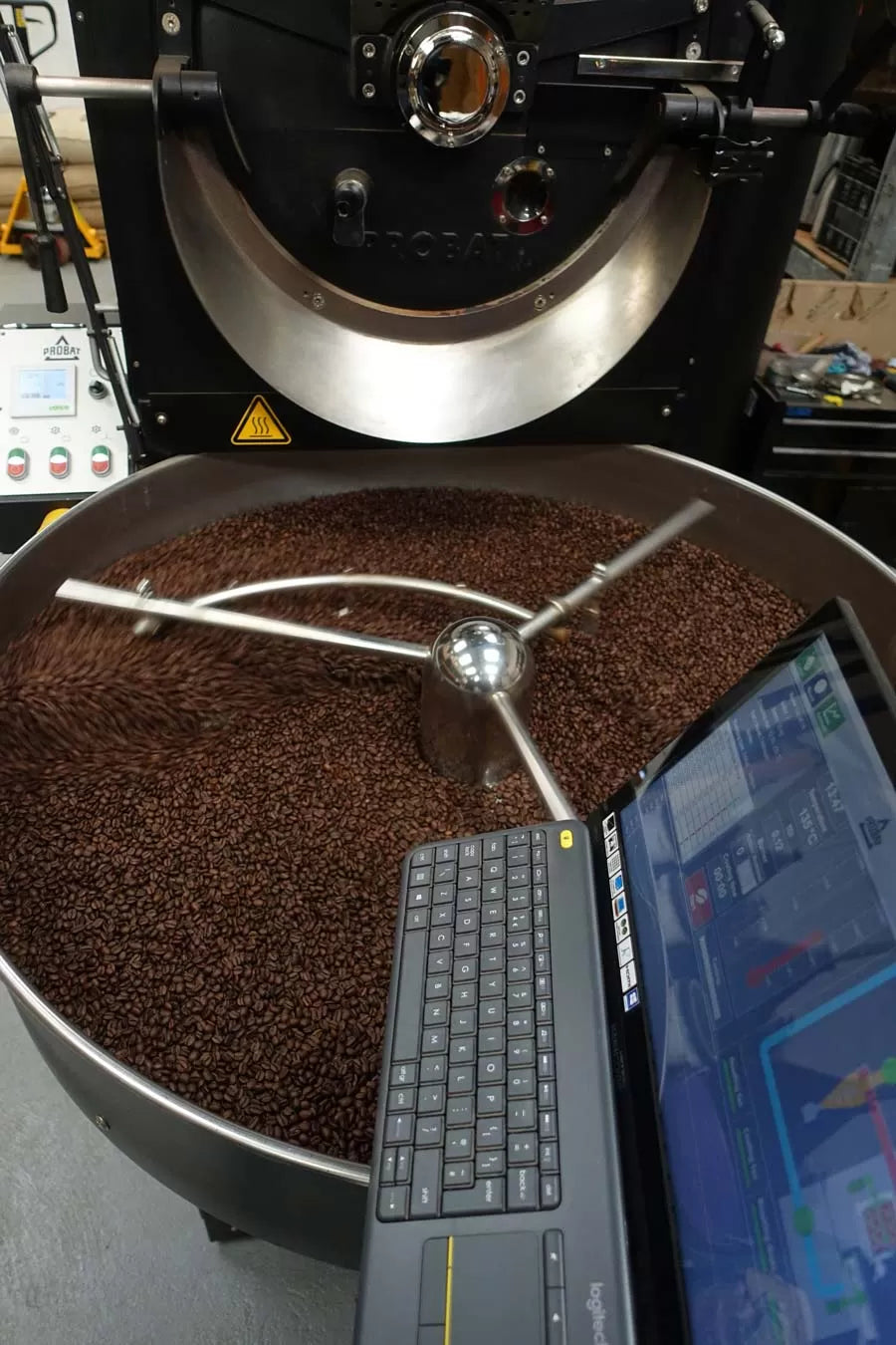 Coffee roasting machine with coffee beans and a laptop displaying software interface.
