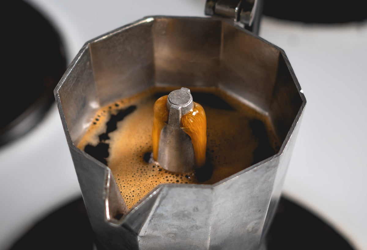 Metal espresso pot with coffee being brewed on a white background