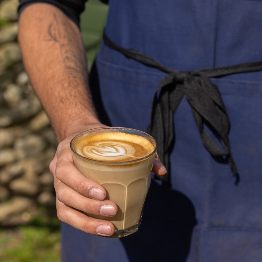 Person holding a glass of cappuccino with a stone wall in the background