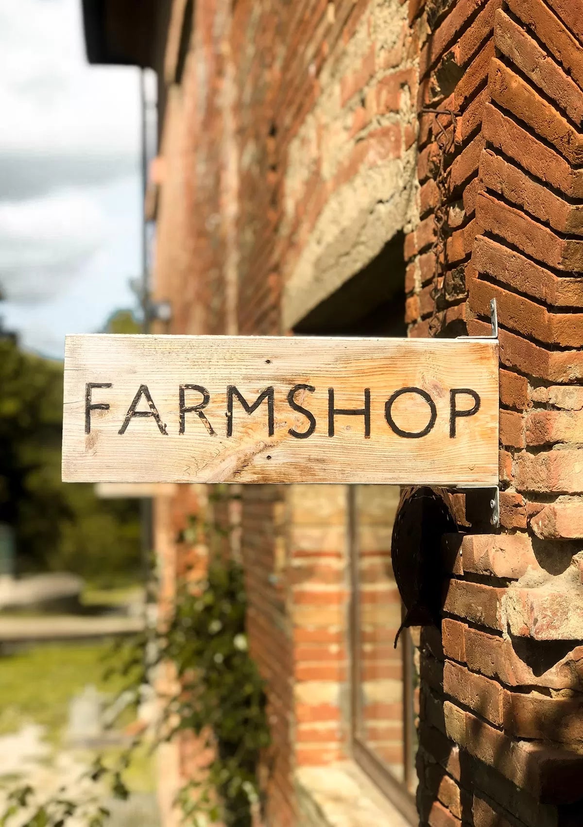 Wooden sign reading 'Farmshop' attached to a brick building.